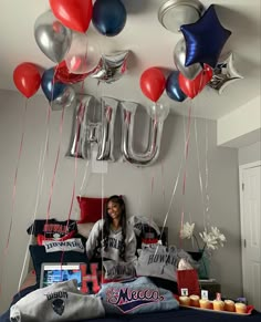 a woman sitting on top of a bed surrounded by red, white and blue balloons