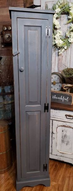 a tall gray cabinet sitting on top of a hard wood floor next to a vase with flowers