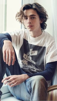 a young man sitting on top of a window sill wearing jeans and a t - shirt