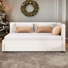 a white daybed with pillows in front of a christmas tree and wreath on the wall