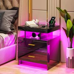 a night stand with a phone on it next to a bed and a potted plant