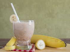 a smoothie in a glass next to bananas and a banana peel on a table