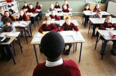 a classroom full of children sitting at desks with their backs turned to the camera