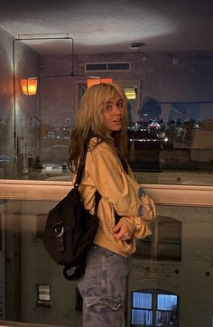 a woman standing in front of a window with a handbag on her shoulder and looking out the window