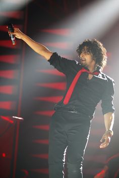 a male in a black shirt and red tie is on stage with his arms out