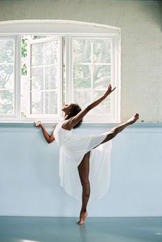 a woman in white dress standing on one leg with her arms stretched out and legs crossed