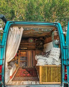 the back end of a blue van filled with furniture and rugs, sitting on top of a wooden floor