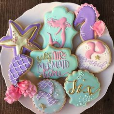 some decorated cookies on a white plate with pink, purple and blue icing in the shape of mermaids