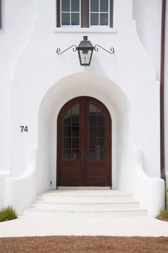 the front entrance to a white building with two brown doors and steps leading up to it