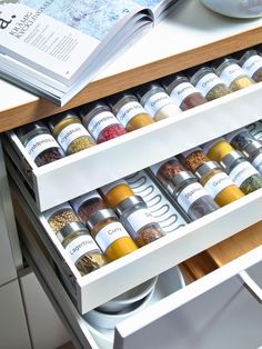 an open drawer with spices in it on top of a kitchen counter next to a book