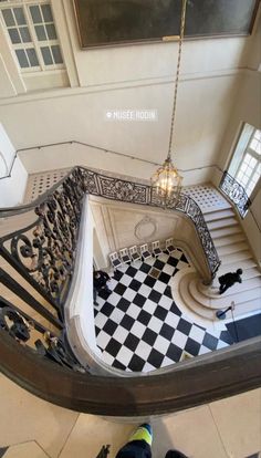 an ornate staircase with black and white checkered flooring, chandelier hanging from the ceiling