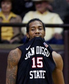 a man with tattoos on his arm holding a basketball in front of him and wearing a jersey that says san diego 15 state