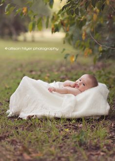 a baby wrapped up in a blanket laying on the ground under a tree with leaves