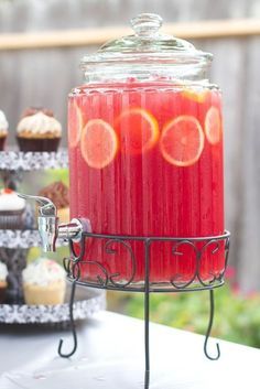 a glass jar filled with red liquid sitting on top of a table next to cupcakes