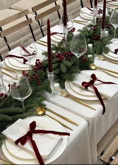 the table is set with white plates, silverware and red bows on them for christmas dinner