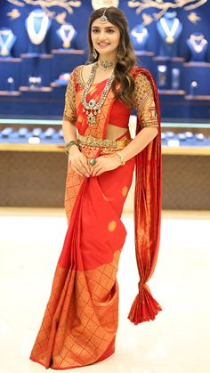 a woman in an orange and red sari posing for the camera with her hands on her hips