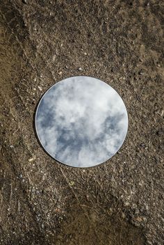 a round mirror sitting on the ground with clouds reflected in it's side view