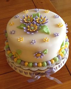 a white cake with flowers on it sitting on top of a wooden table next to a ribbon