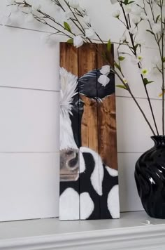 a vase with flowers sitting on top of a mantle next to a wooden sign that says cow