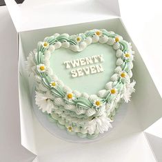 a heart shaped cake with the words twenty seven written in frosting and daisies