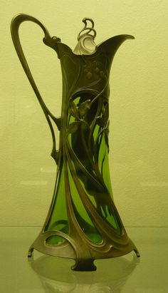 a green glass vase sitting on top of a table next to a white wall and floor