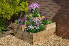 a wooden planter filled with lots of flowers next to a brick wall and shrubbery