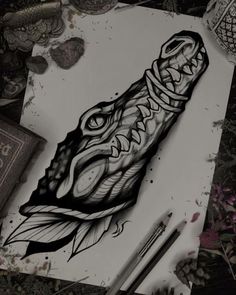 a drawing of an alligator's head on paper next to pencils and flowers