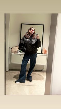 a woman taking a selfie in front of a mirror wearing jeans and a leather jacket