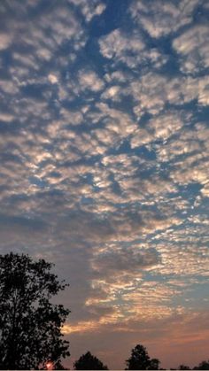 the sky is filled with clouds as the sun sets in the distance behind some trees