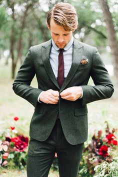 a man in a suit and tie is looking down at his pocket while standing outside