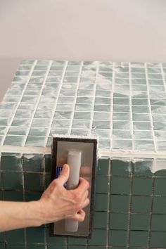 a person is holding a toothbrush in front of a green tiled box with an opening