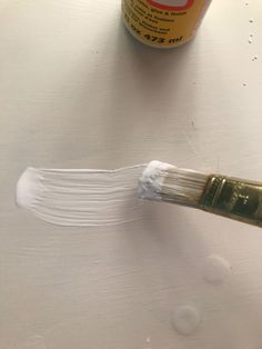 a paintbrush with white bristles on it next to a can of brown and white acrylic