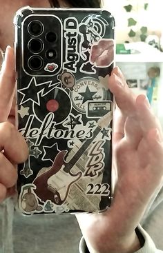 a person holding up a cell phone case with stickers all over it and an image of a guitar