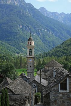 a clock tower in the middle of an old village with mountains in the back ground