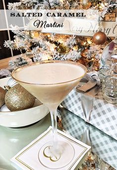 a table topped with a martini glass filled with liquid next to a christmas tree covered in ornaments