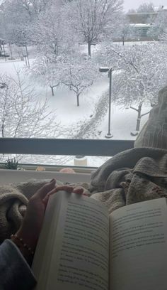 someone is reading a book while sitting in the window sill on a snowy day