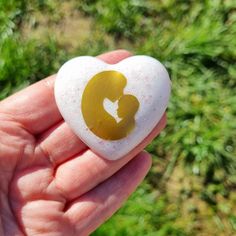 a hand holding a heart shaped rock with a gold silhouette on it