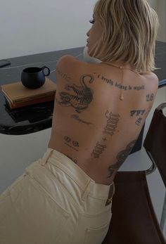 a woman with tattoos on her back sitting in front of a table and coffee cup