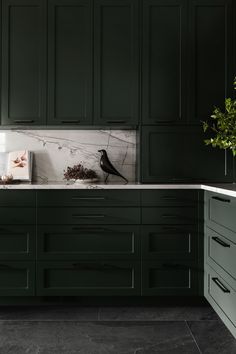 a kitchen with dark green cabinets and marble counter tops, along with a black bird on the wall