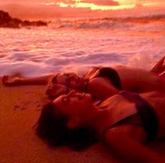 two people laying on the beach at sunset