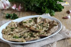 a white plate topped with meat covered in gravy next to garlic and parsley