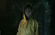 a young boy wearing a yellow raincoat standing in the dark with his hands on his hips