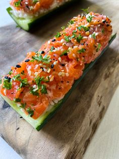 two cucumbers with salmon and herbs on them sitting on a wooden cutting board