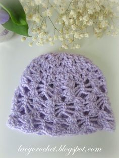 a crocheted hat sitting on top of a table next to a white flower