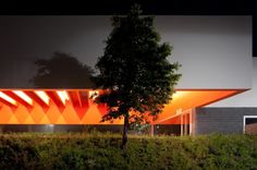 an orange building is lit up at night with trees in the foreground and bushes to the side