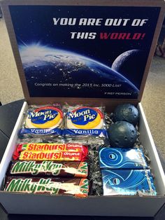 an open box filled with candy on top of a table next to a sign that says you are out of this world