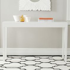 a white table sitting in front of a mirror on top of a wall next to a black and white rug