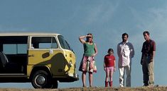 three adults and two children are standing in front of a van on the side of a hill