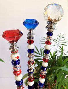 three colorful glass candlesticks sitting on top of a table next to a potted plant