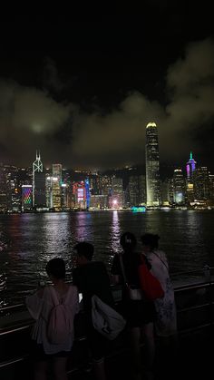 some people are standing by the water and looking at the city lights in the distance